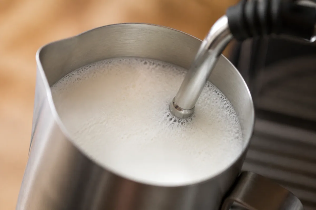 Buse vapeur plongée sous la surface du lait à environ 1,5 cm, pichet incliné