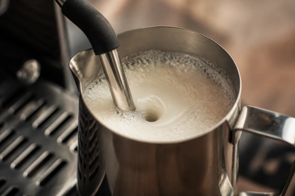 Buse vapeur créant un vortex dans un pichet inox, surface du lait avec microbulle